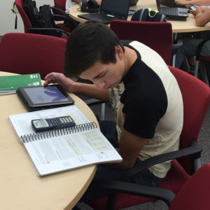 student looking at book while using tablet